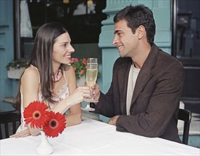 Hispanic couple toasting with champagne at outdoor cafe