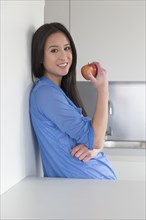 Mixed race woman eating fruit in kitchen