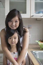 Asian mother hugging daughter in kitchen