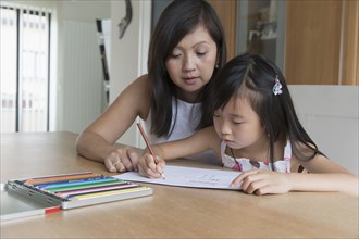Asian mother watching daughter coloring