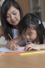 Asian mother watching daughter coloring