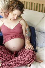 Caucasian pregnant lesbian couple relaxing on bed