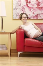 Caucasian pregnant woman having cup of coffee on sofa