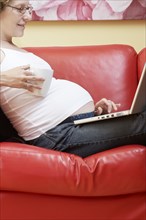 Caucasian pregnant woman using laptop on sofa
