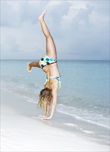 Caucasian woman doing cartwheels on beach