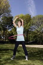 Mixed race woman spinning with plastic hoop in park
