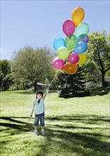 Mixed race girl holding bunch of balloons in park