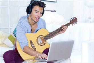 Mixed race teenager playing guitar and using laptop