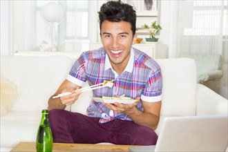 Mixed race teenager eating sushi on sofa