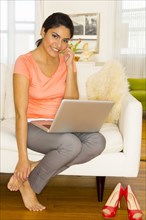 Hispanic woman using laptop and cell phone on sofa