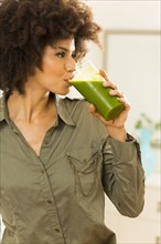 Mixed race woman drinking green smoothie