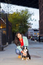 Mixed race woman petting dog on city sidewalk