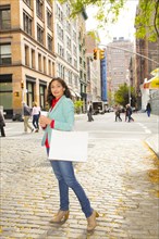 Mixed race woman with shopping bag on city street