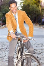 Mixed race businessman riding bicycle on city street