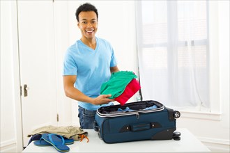 Mixed race man packing suitcase