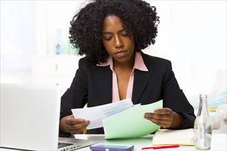 Mixed race businesswoman reading papers at desk