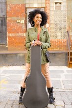 Mixed race woman with guitar case on city street