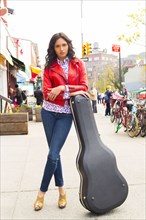 Mixed race woman with guitar case on city sidewalk