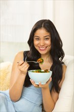 Hispanic woman eating salad on sofa