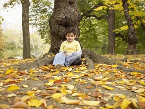 Hispanic boy sitting near tree in autumn