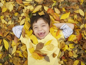 Toothless Hispanic boy laying in autumn leaves