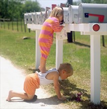 Girl standing on brother's back and peering into mailbox