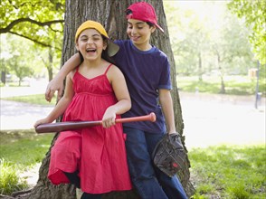 Smiling mixed race brother and sister holding baseball bat and mitt