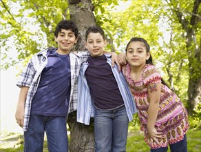 Mixed race boys and girl hugging in front of tree
