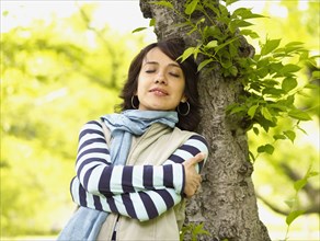 Hispanic woman leaning against tree with eyes closed
