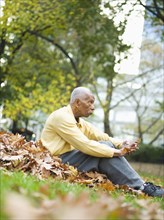 Senior man sits in autumn leaves in park