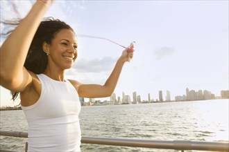 Smiling Hispanic woman jump roping at waterfront