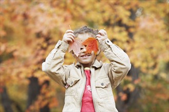 Hispanic girl holding autumn leaves over her eyes