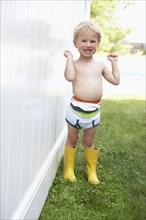 Caucasian boy wearing diaper and rain boots outdoors