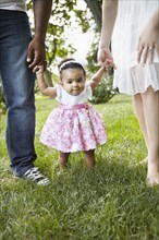 Parents helping daughter walk in park