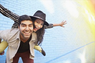 Indian couple piggybacking along brick wall