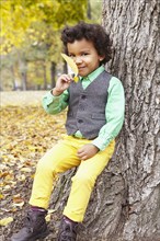 Mixed race boy holding leaf in park