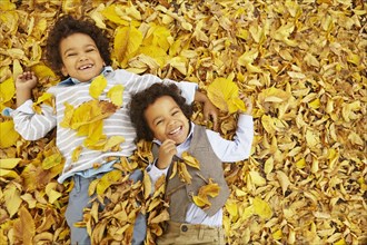 Mixed race boys laying in yellow autumn leaves