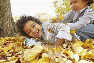 Mixed race boys playing in yellow autumn leaves