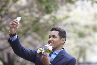 Man in suit taking cell phone selfie while holding flowers