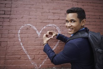 Smiling man making heart shape with hands by heart chalk drawing on wall