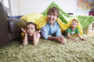 Father and children playing in blanket fort in living room
