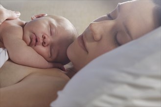 Mother sleeping with newborn baby on bed