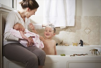 Caucasian mother and newborn washing son in bath