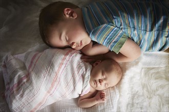 Boy napping with newborn sibling on bed