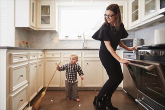 Caucasian mother and son holding broom kitchen