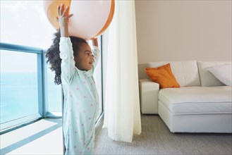 Black girl playing with beach ball in living room