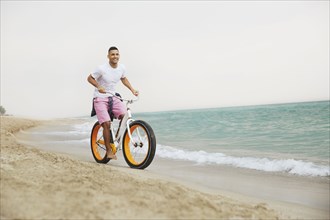 Black man riding bicycle on beach