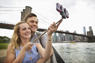 Caucasian couple taking selfie with cell phone under Brooklyn Bridge
