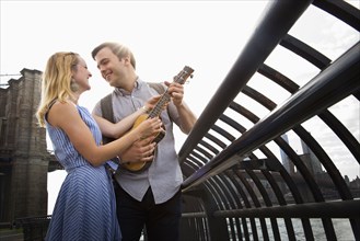 Caucasian couple playing ukulele on urban waterfront