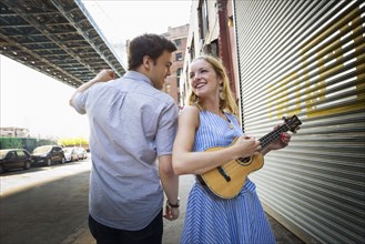 Caucasian couple playing ukulele in city